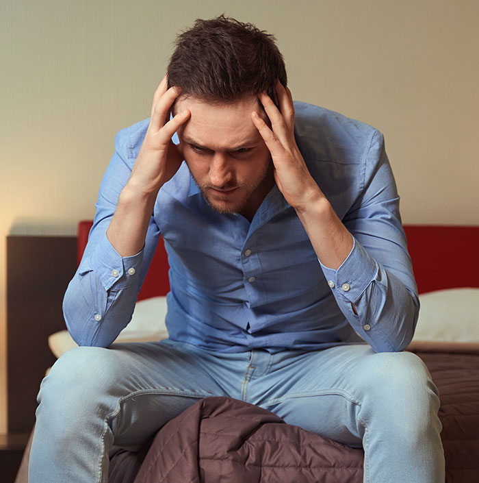 Man in a blue shirt sitting on a bed, looking frustrated, concerned about religion and relationship choices.