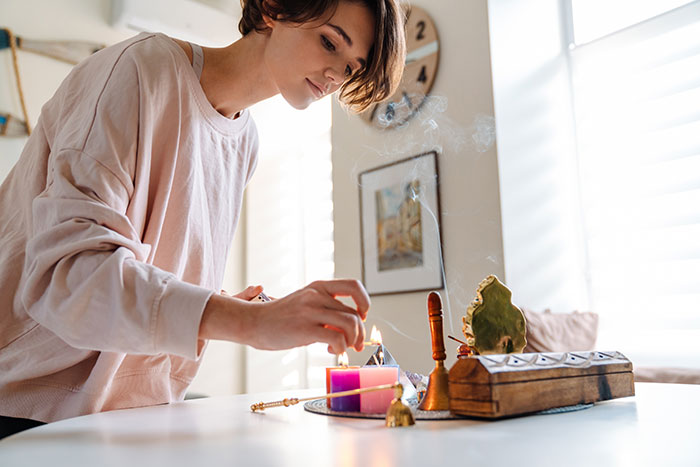 Woman lighting incense at home, engaging in a religious practice.