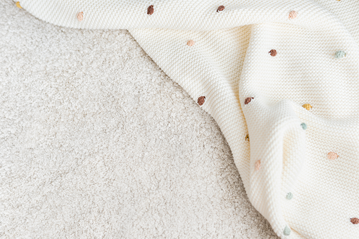 A soft baby blanket with colorful dots partially spread out on a textured surface.