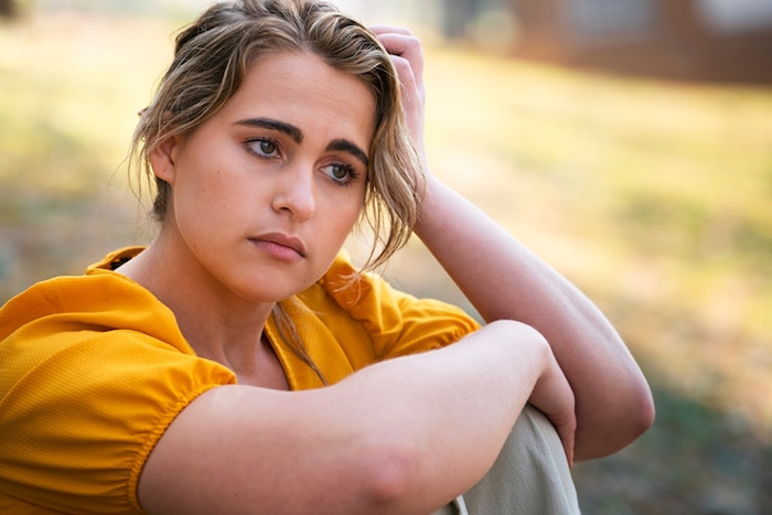 Woman looking distraught, sitting outside in a yellow blouse, reflecting on her attachment to a baby blanket.