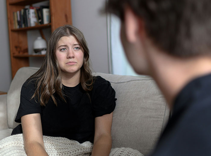 A woman on a couch looks upset, engaging in a serious conversation with a man, illustrating a "nice guy" encounter.
