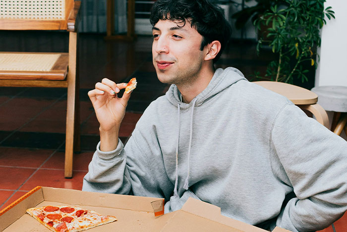 Man in a gray hoodie enjoying pizza, representing the "nice guys" theme in everyday settings.