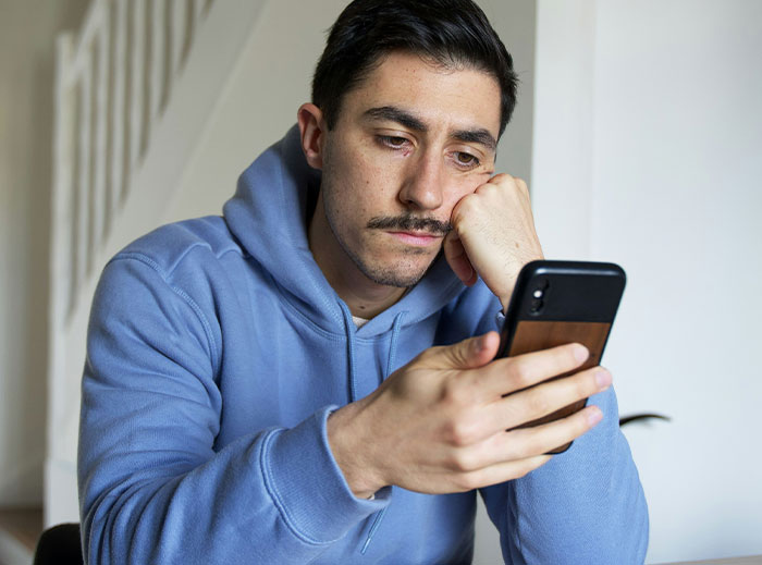 Man in blue hoodie looking at his phone with a thoughtful expression, related to stories about "nice guys."