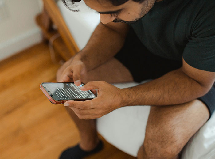 Man in casual wear sitting and looking intently at a smartphone.