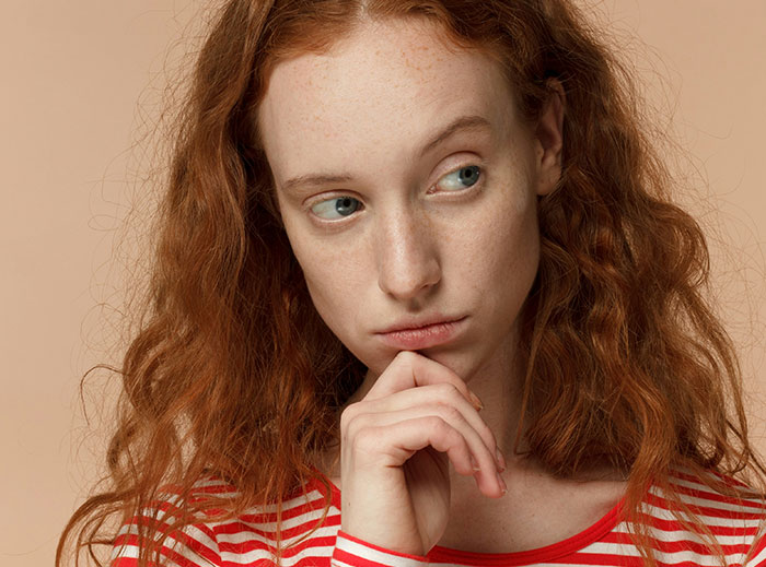 Woman with wavy red hair and a pensive look, wearing a red and white striped shirt; concept of "nice guys" skepticism.