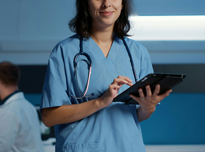 Healthcare professional in blue scrubs using a tablet in a medical setting.