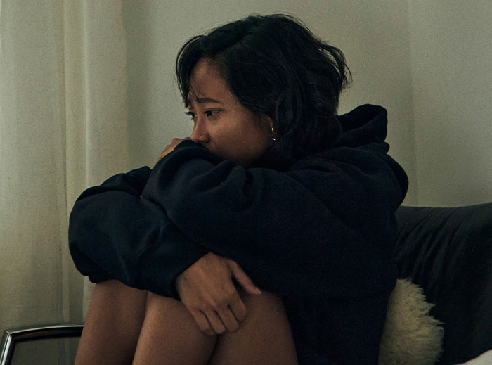 A woman sitting on a couch, looking contemplative and wrapped in a hoodie, related to creepy stories about "nice guys".