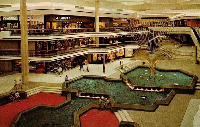 Vintage mall interior with a fountain and shoppers, evoking nostalgia for classic shopping centers.