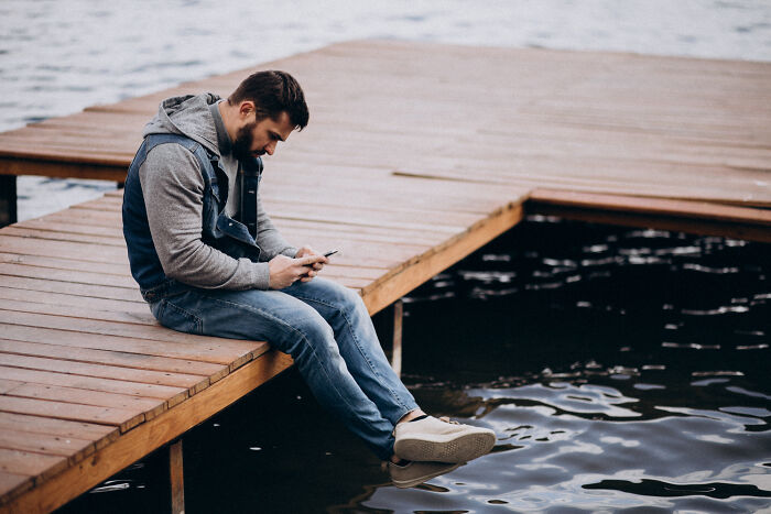 Man on dock looking at phone beside water; an insignificant thing stuck in thought.