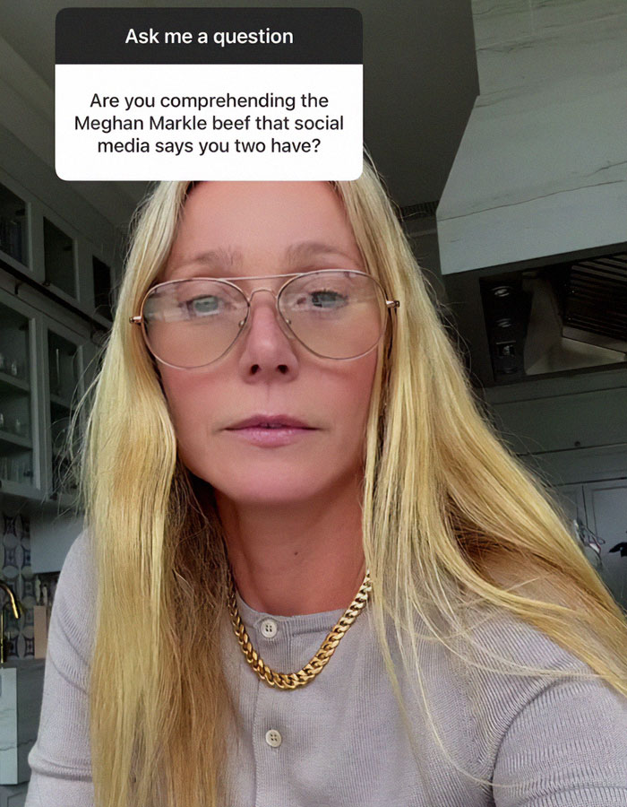 Blonde woman with glasses and gold chain responds to Meghan Markle feud rumors in a casual setting.