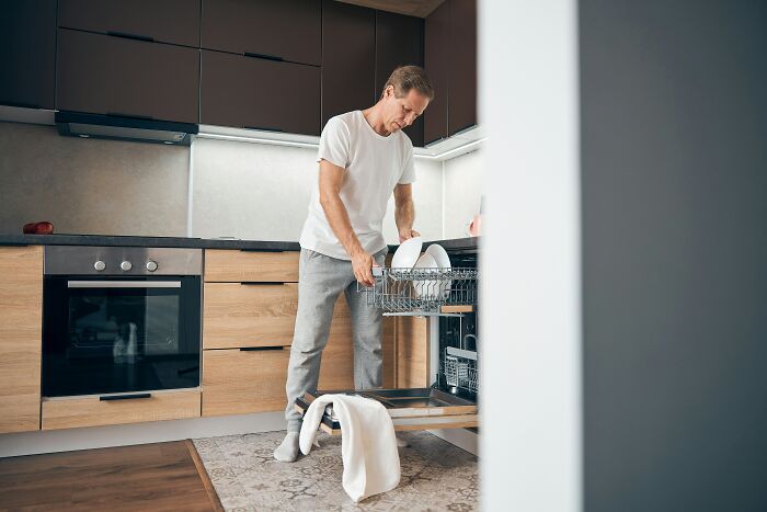 Man unloading dishwasher in a modern kitchen, demonstrating effective cleaning hacks.