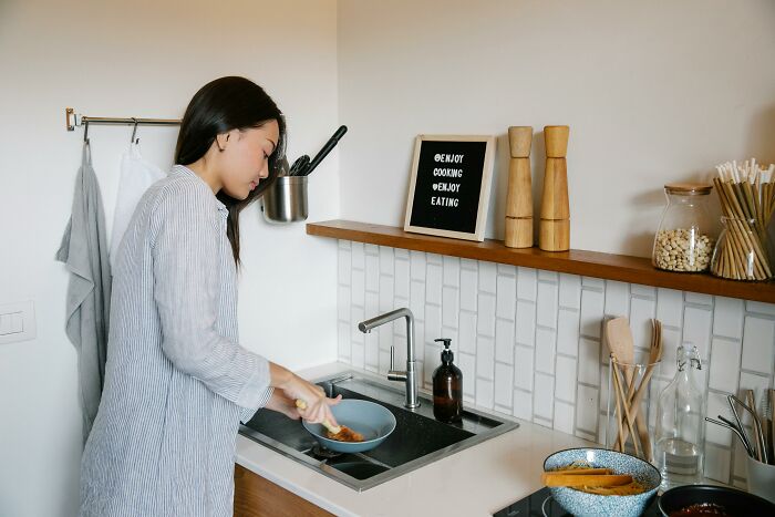 Woman using a kitchen cleaning hack at the sink, wearing striped apparel, with spices and utensils on the counter.