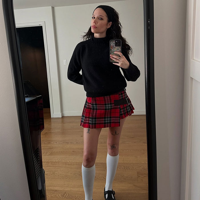 Singer taking a mirror selfie in a plaid skirt and black sweater, addressing critics of her bold photos. Singer taking a mirror selfie in a plaid skirt and black sweater, addressing critics of her bold photos.