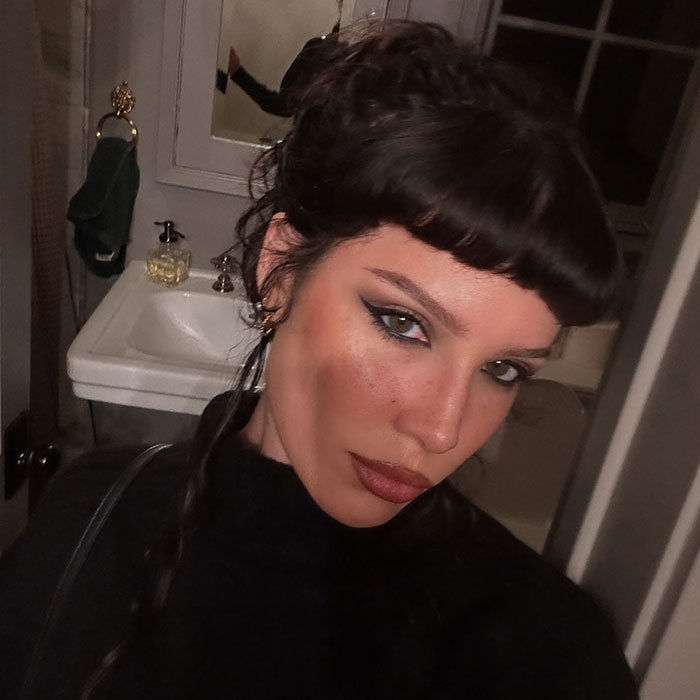 A woman with dark hair and makeup in a bathroom, capturing a selfie. A woman with dark hair and makeup in a bathroom, capturing a selfie.