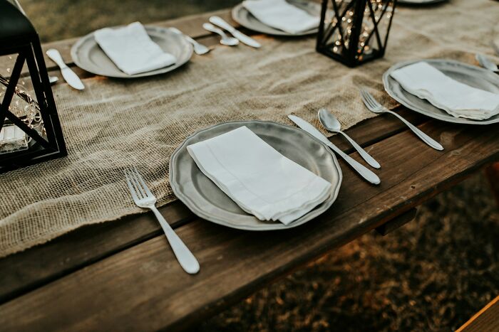 Wedding table setting with plates, cutlery, and lanterns on a burlap runner, capturing a rustic yet elegant theme.