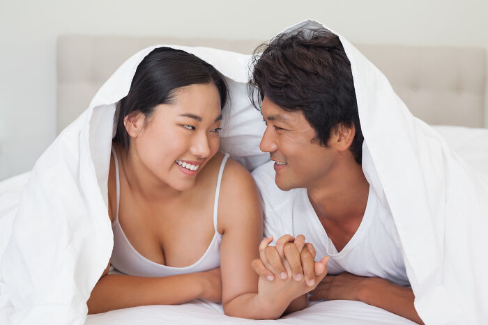 Couple under a white blanket, smiling and holding hands, conveying historical facts theme.