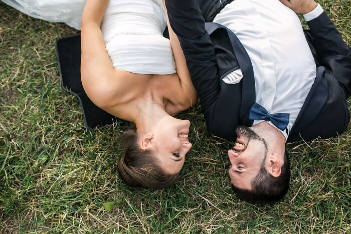 Bride and groom lying on grass, sharing a smile after a wedding nightmare experience.