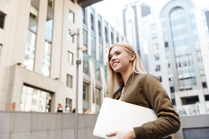 Young woman holding a laptop outside a university building, symbolizing free tuition announcement at Harvard. Young woman holding a laptop outside a university building, symbolizing free tuition announcement at Harvard.