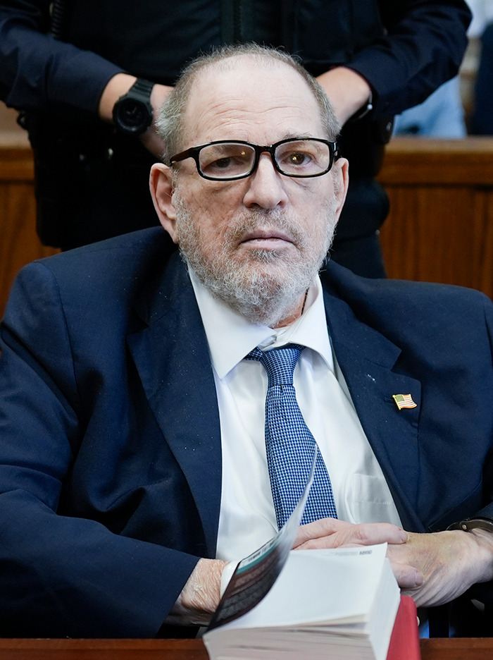 Harvey Weinstein in a suit and glasses sits in a courtroom.