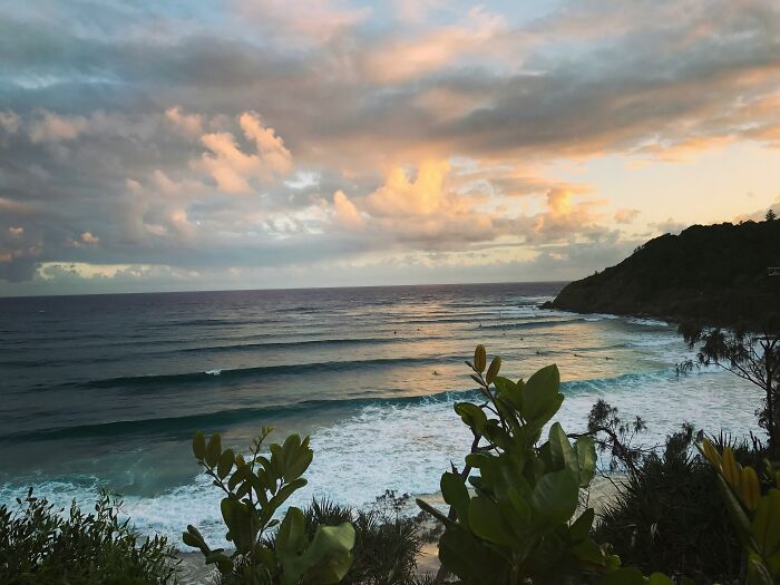 Sunset over a stunning beach with gentle waves and lush greenery in the foreground.