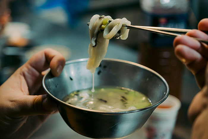 Person holding chopsticks above a metal bowl in a restaurant kitchen.