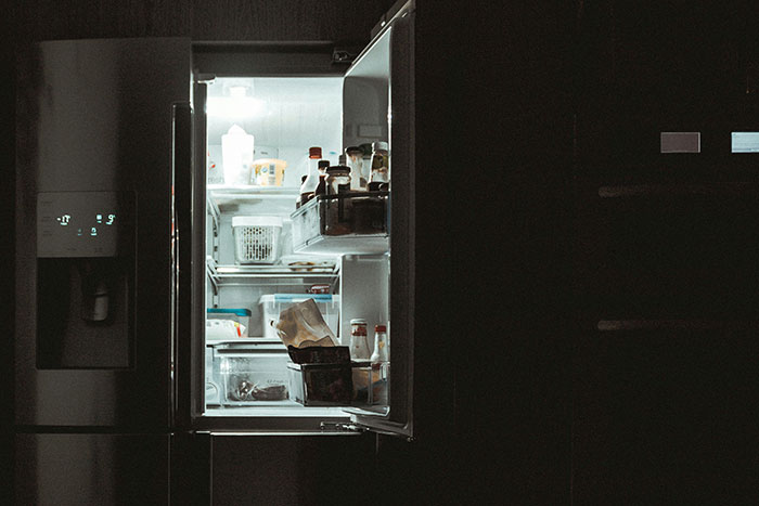 Open refrigerator in a dimly lit kitchen with assorted food items, highlighting restaurant kitchen conditions.