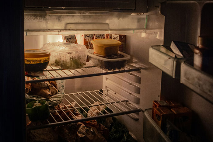 A messy restaurant kitchen fridge with cluttered containers and food items.