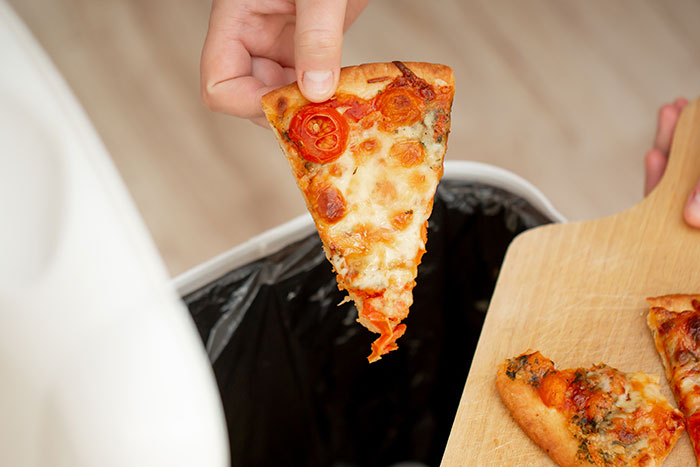 Hand disposing of a pizza slice, illustrating restaurant kitchen issues and hygiene concerns.