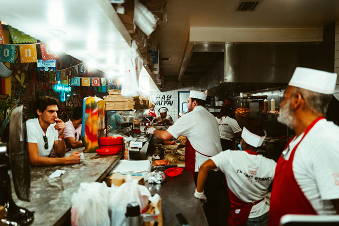 Restaurant kitchen staff in action, wearing uniforms, busy preparing food behind a counter.
