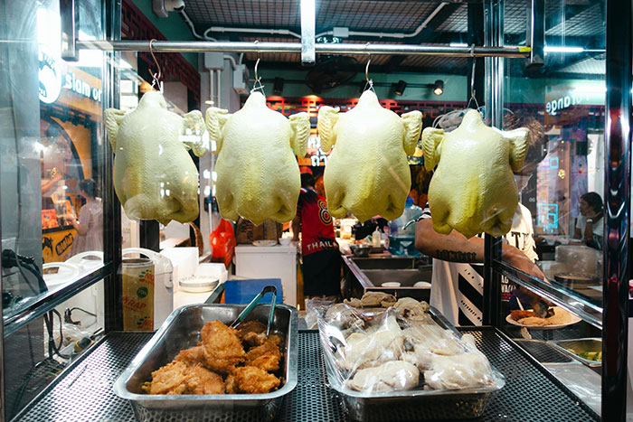 Restaurant kitchen with whole chickens hanging, fried food, and buns displayed.