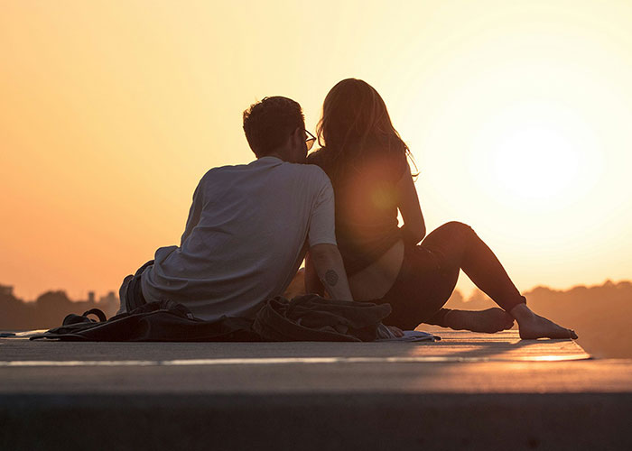A couple sitting close at sunset, suggesting they might be more than "just friends."