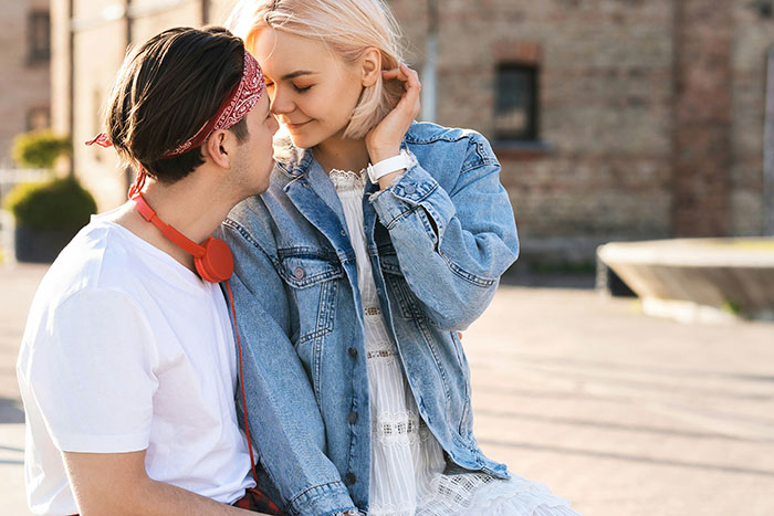 A couple sits closely, embracing in a flirty manner, outdoors.