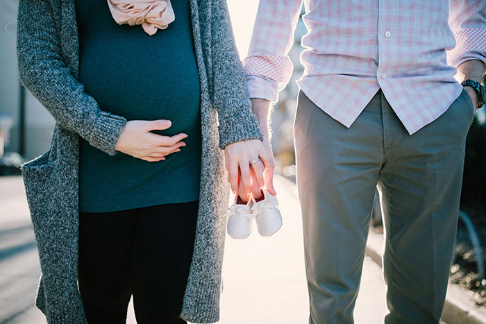 Pregnant woman holding partner's hand, with baby shoes, suggesting more than just friends.