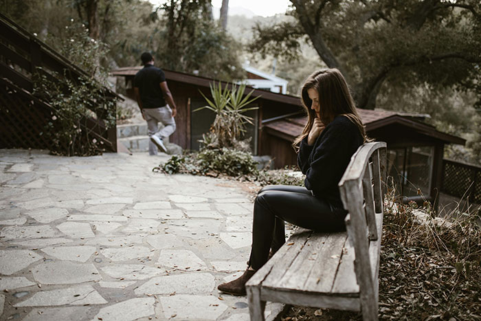 A woman sitting on a bench looking thoughtful while a man walks away, depicting a "just a friend" scenario.