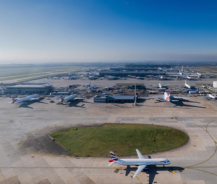 Heathrow Airport tarmac with parked planes under a clear blue sky, highlighting flight disruptions. 