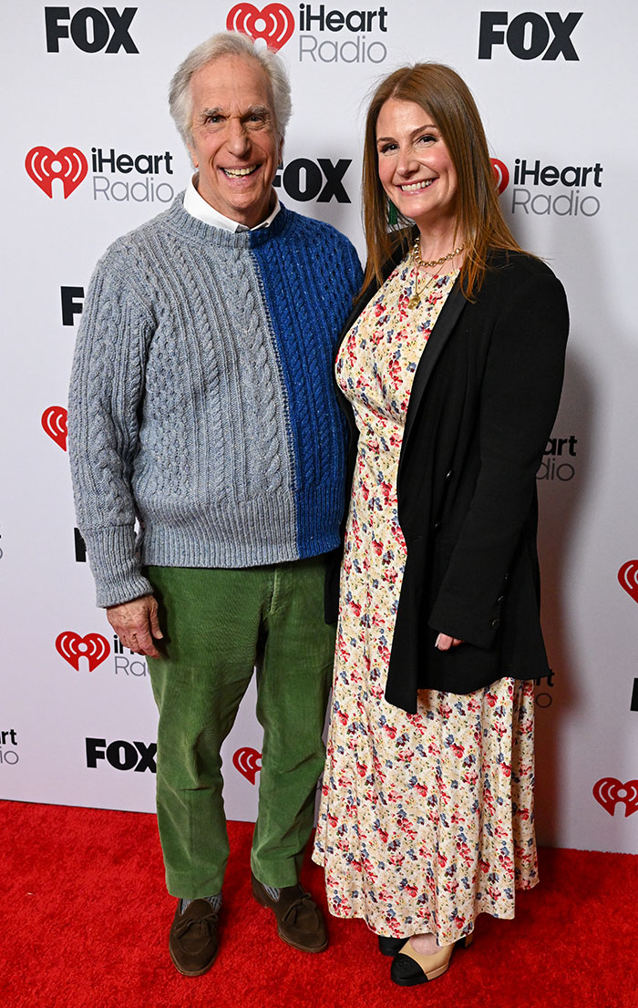 Two people smiling on the red carpet at the 2025 iHeartRadio Music Awards, wearing casual outfits.