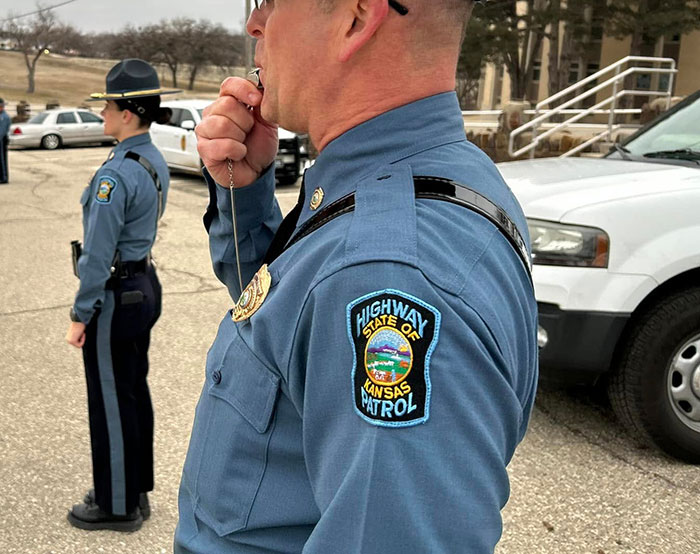 Kansas trooper in uniform with patrol badge, standing beside a vehicle, illustrating a rescue story. Kansas trooper in uniform with patrol badge, standing beside a vehicle, illustrating a rescue story.