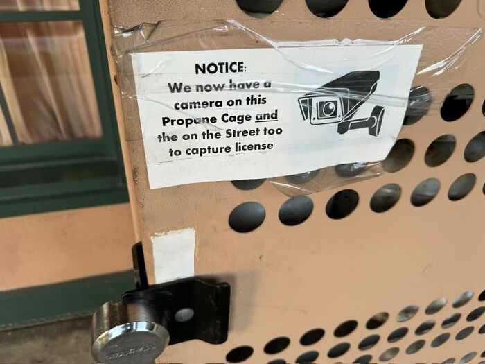 Sign on wall warns about camera surveillance on propane cage after a big mistake.