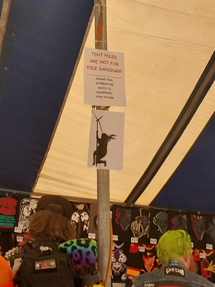 Tent pole with warning signs about not pole dancing, people in a colorful setting.