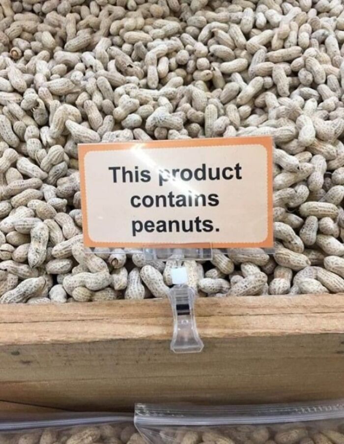 Sign stating "This product contains peanuts" placed on a pile of peanuts, highlighting warning signs and errors.