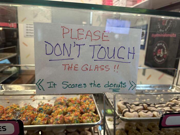 Sign warning not to touch glass as it scares the donuts, a humorous aftermath of a mistake in a bakery.