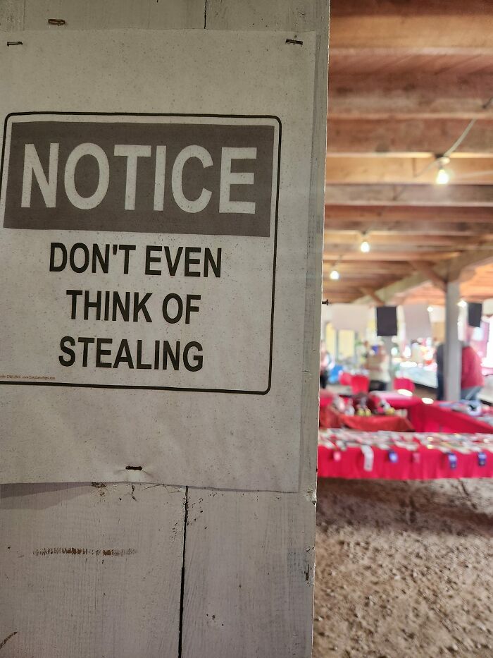 Warning sign in a market saying "Don't even think of stealing" with tables in the background.