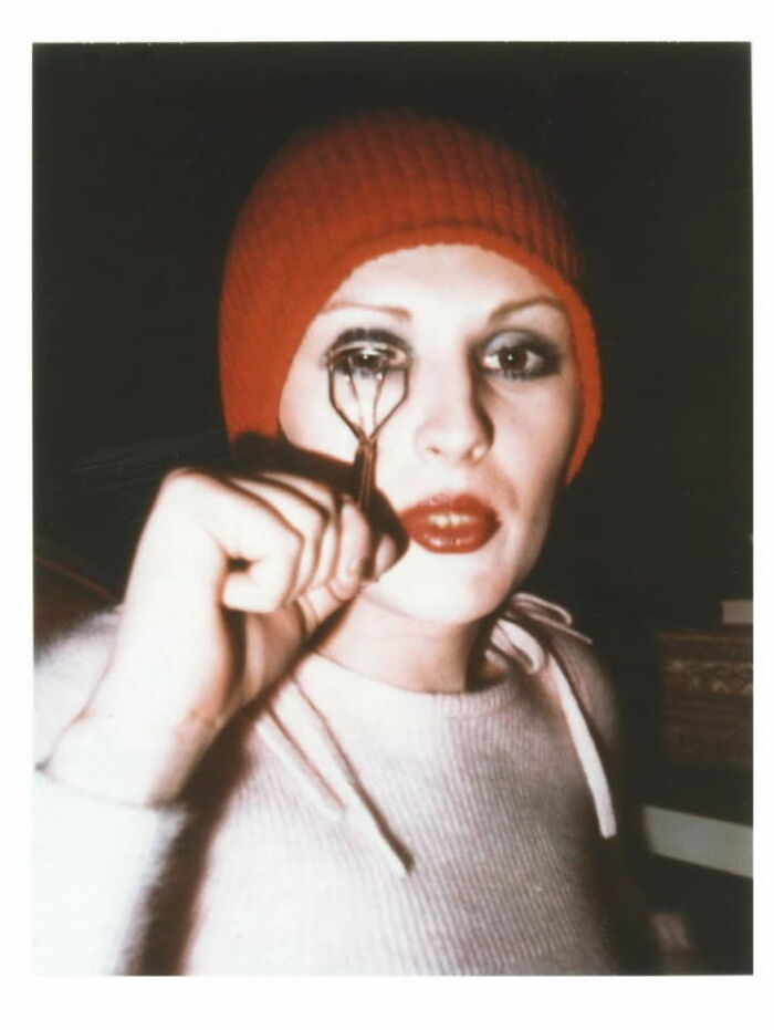 A woman in a red hat using an eyelash curler, showcasing a moment from forgotten corners of history.