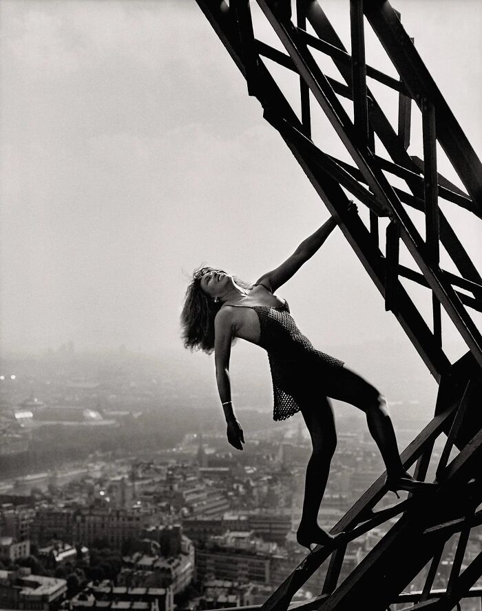 Woman posing on the Eiffel Tower, representing forgotten corners of history with a cityscape in the background.