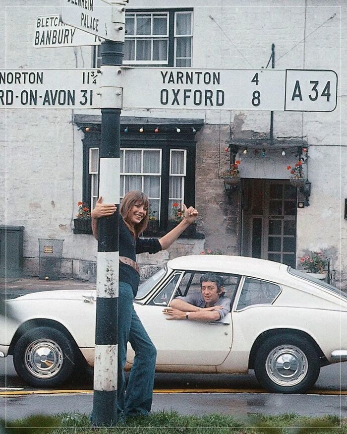 Historic photo of a woman at a road sign with a vintage car; man inside.