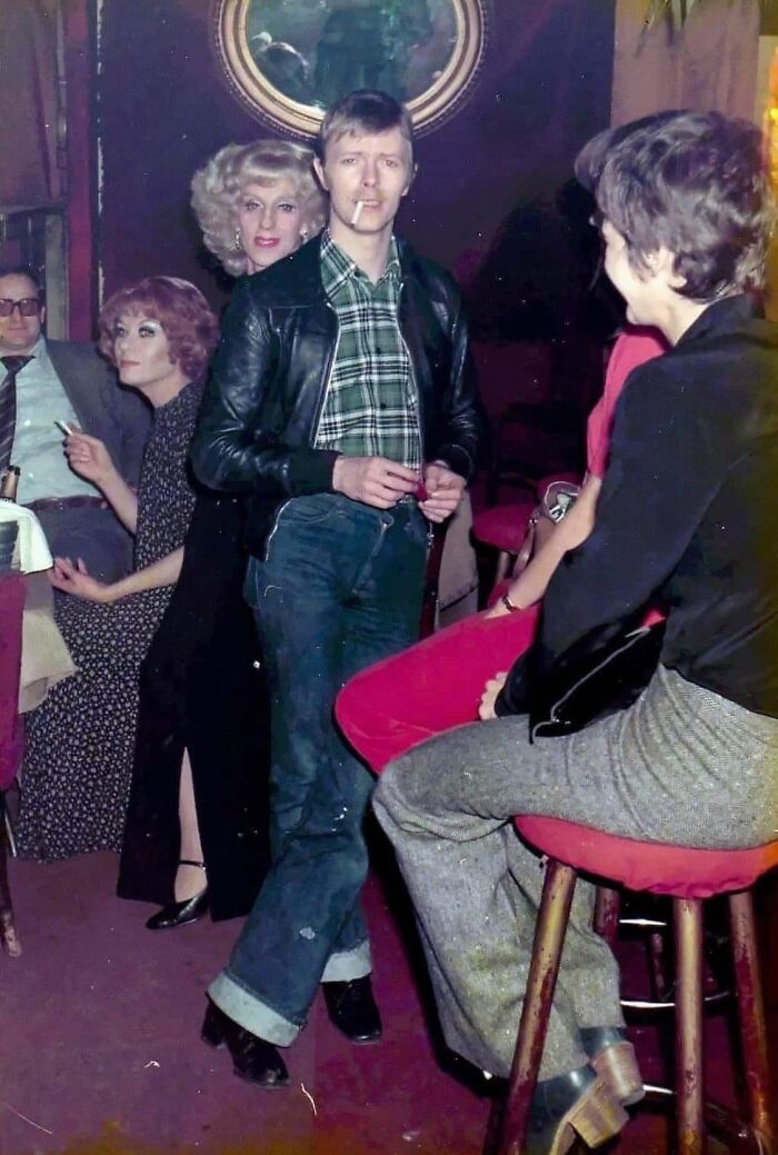 Group at a vintage party with a man in a leather jacket smoking, capturing a forgotten corner of history.