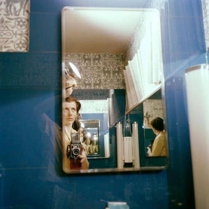 Person with a vintage camera captured in a bathroom mirror, reflecting forgotten history.