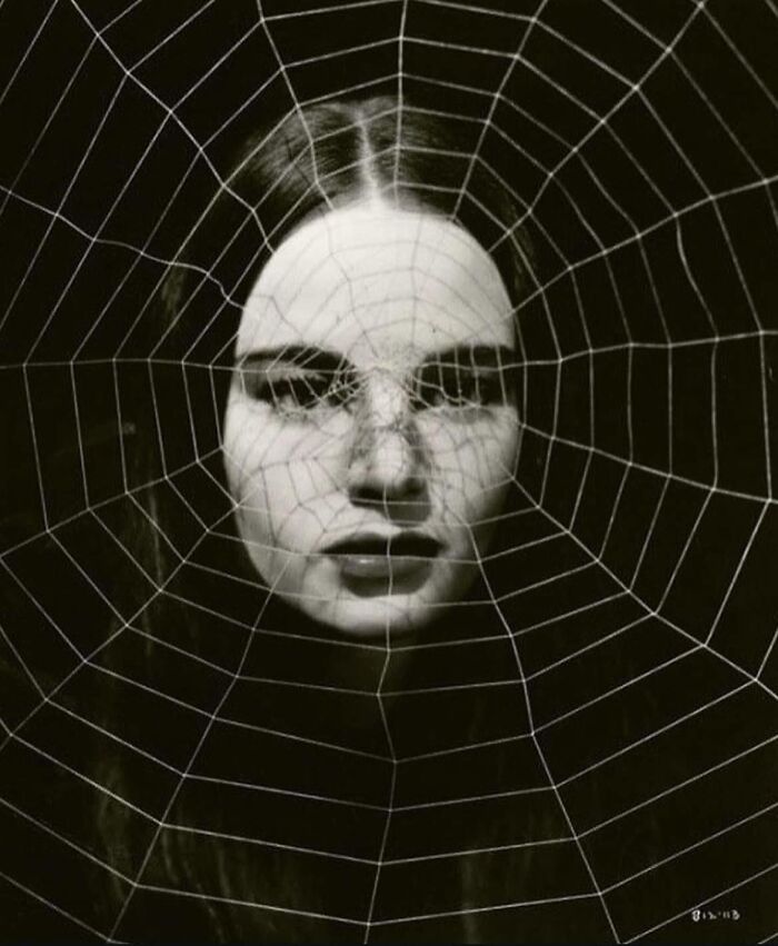 A woman's face behind a spider web, symbolizing forgotten corners of history in a black and white photo.