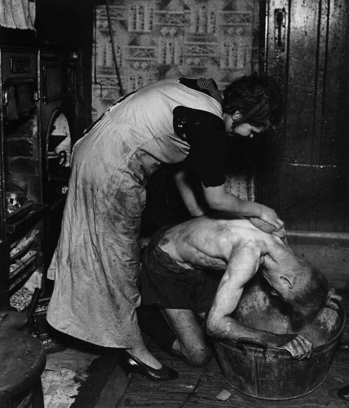 Woman assists with man's bath in a tin tub, showcasing a forgotten corner of history.