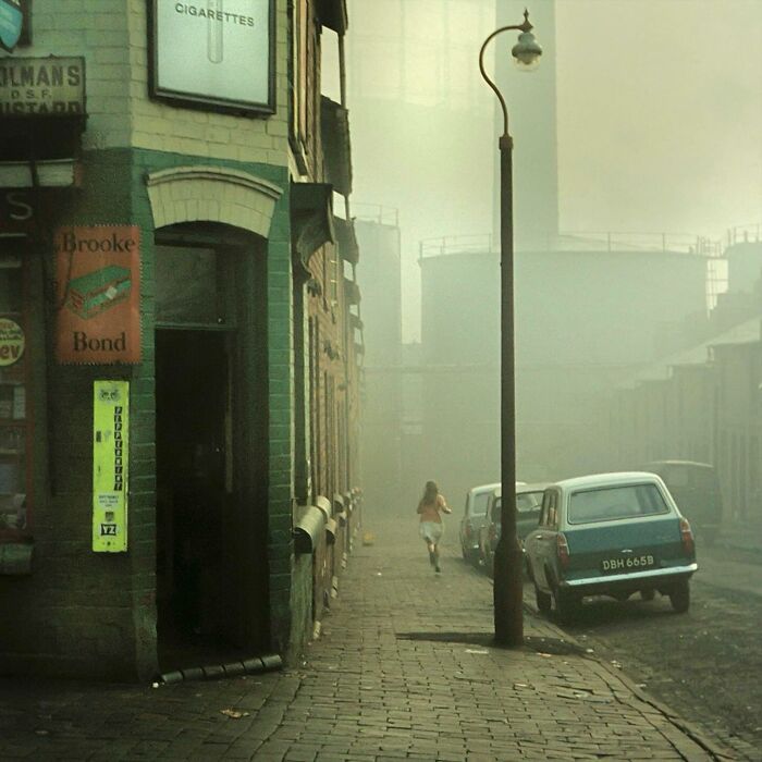 A misty street scene in an industrial city, featuring historical architecture and vintage cars.